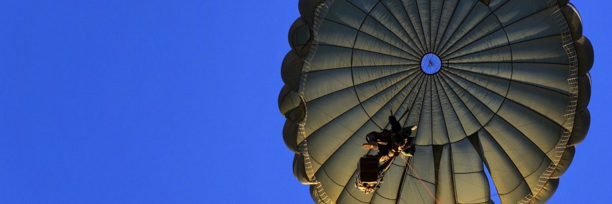 A soldier descends under a round military parachute